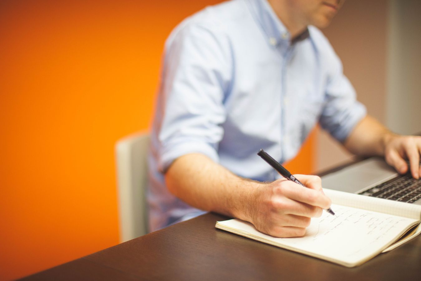 Person writing website content notes beside a laptop